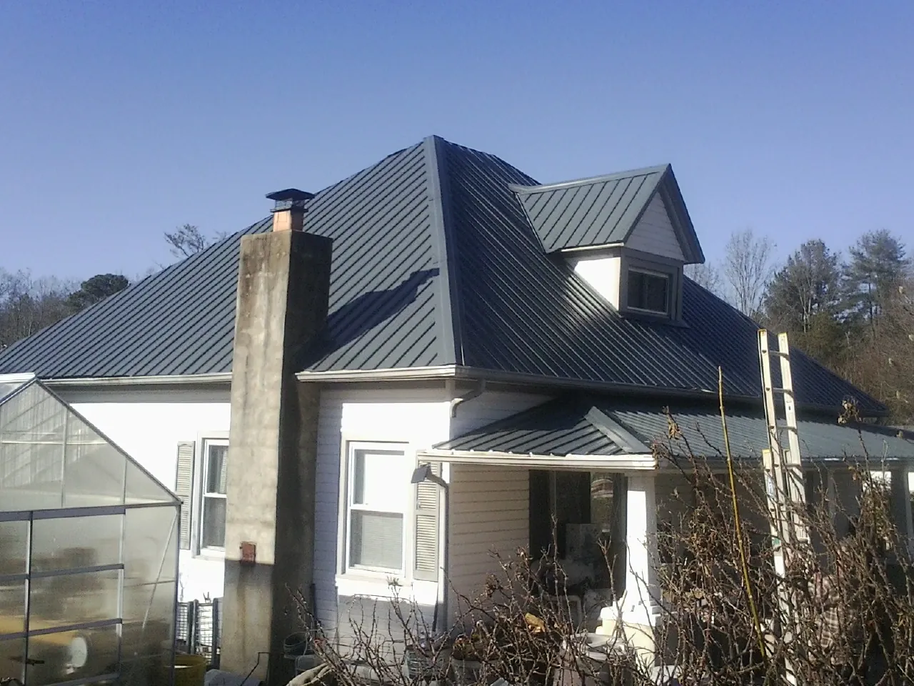 Dark blue standing seam metal roof on a white farmhouse with dormer — Slate & Tile Roof Repair by Roofing Brothers in Brandeis