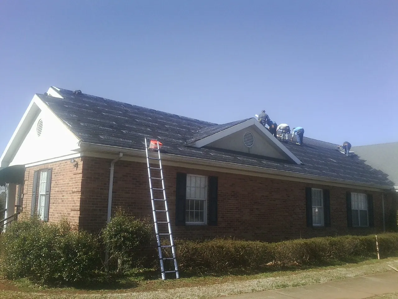 Crew tearing shingles off a brick ranch roof with a ladder set — Emergency Roof Repair work by our crew in Brandeis