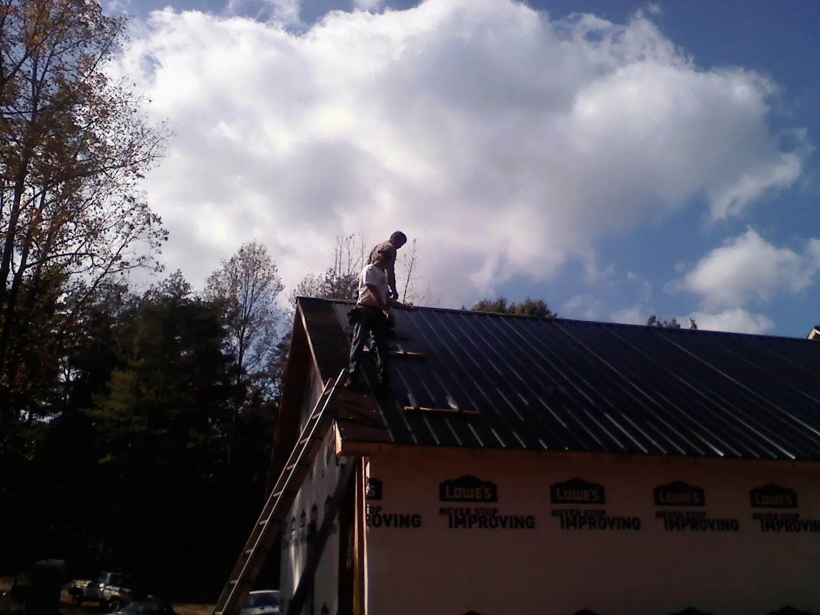 Roofer fastening dark metal panels high against a cloudy sky, from a Roof Inspection job in Brandeis
