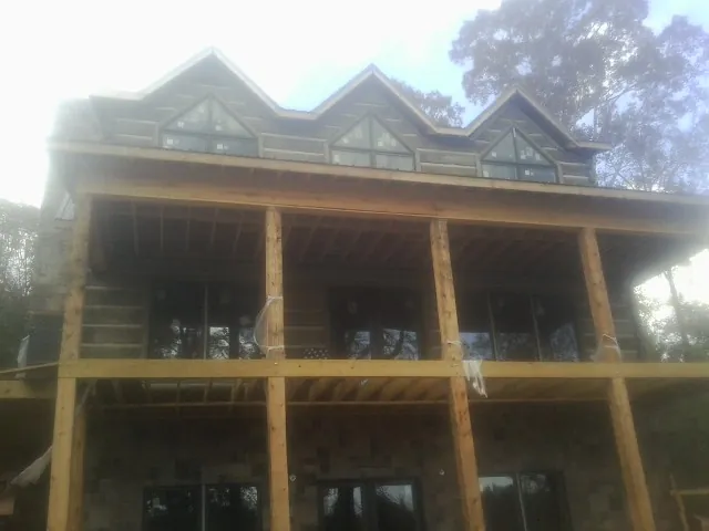 Dormers and porch framing on a large log home under construction — Roof Coating work by our crew in Brandeis